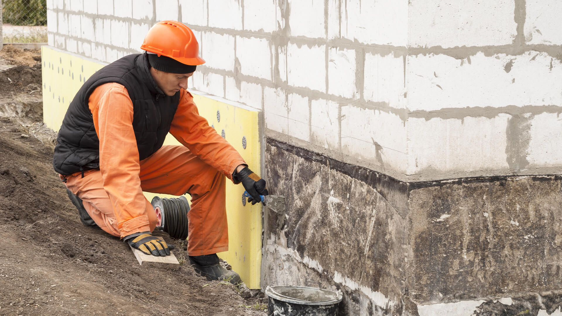 Technician applying moisture protection along a foundation wall
